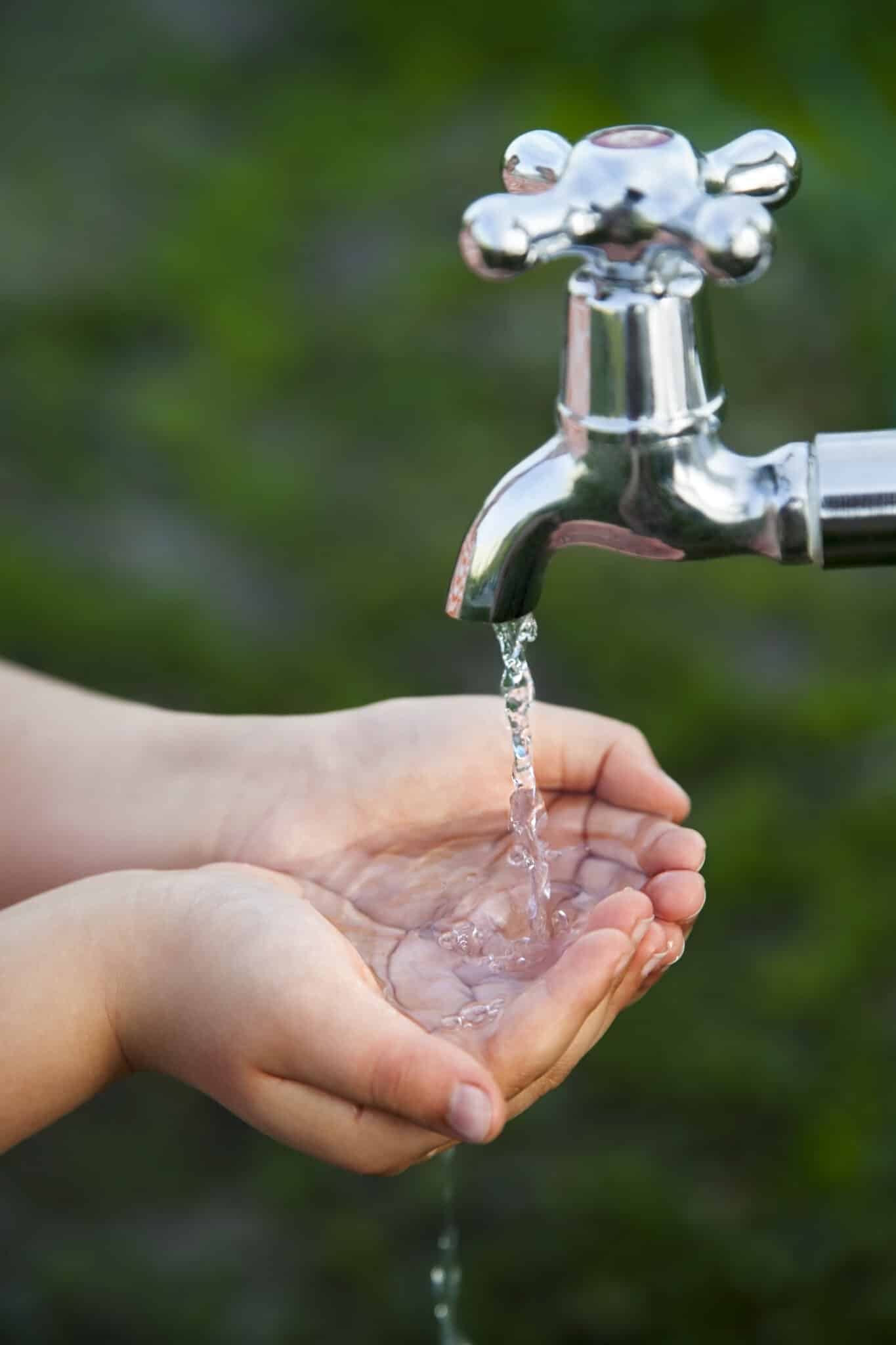 A young boy washing his hands under a garden faucet, symbolizing water efficiency with mindful outdoor water use.