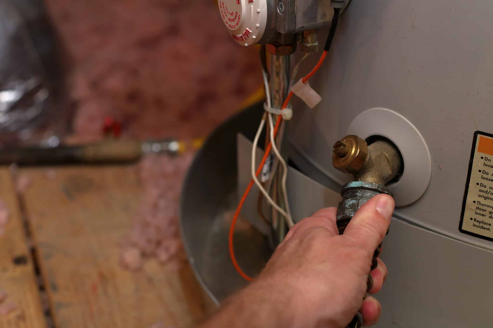 Hand attaches hose to water heater drain to perform Water Heater Repair and maintenance