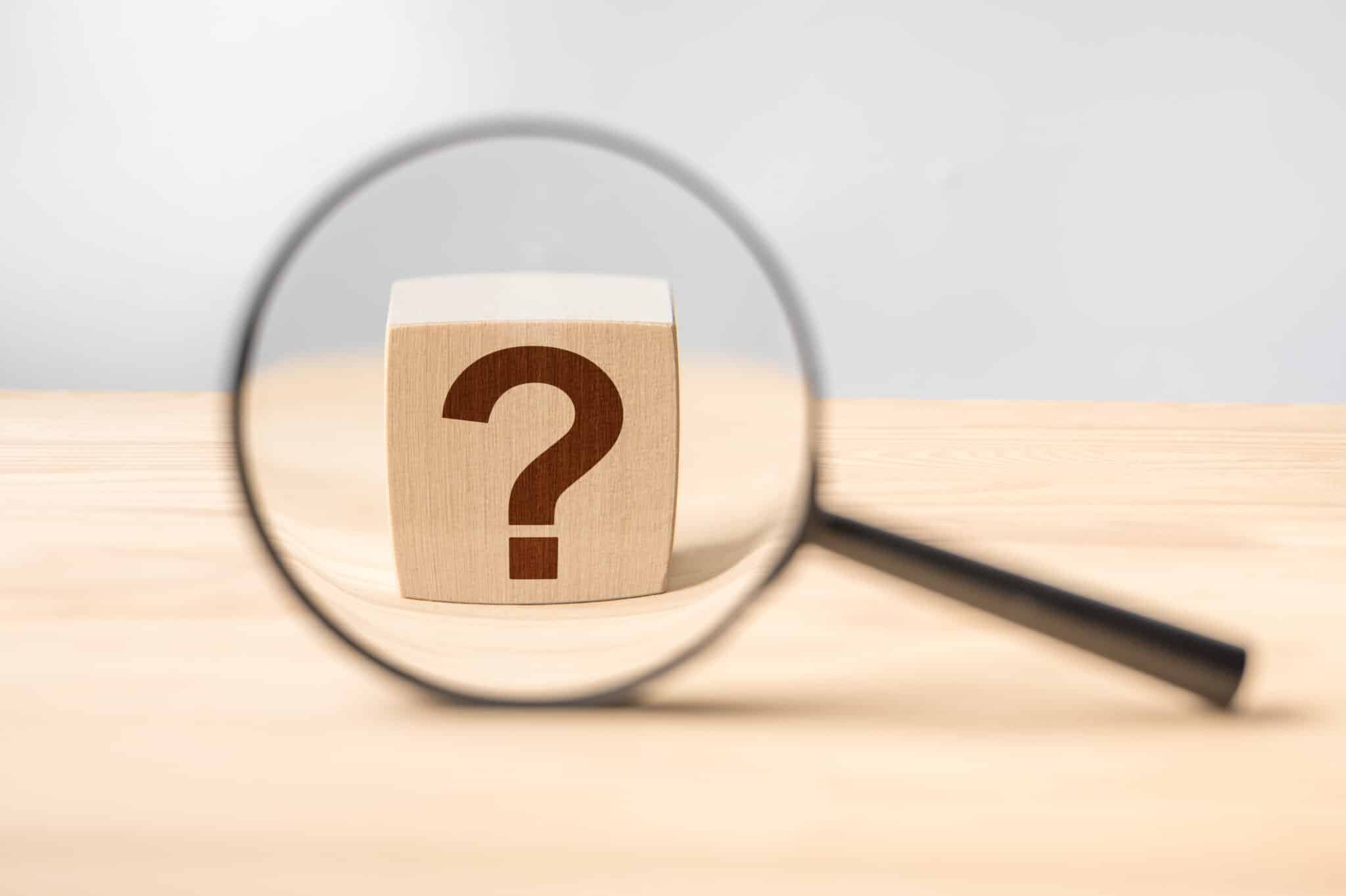 Magnifying glass with question mark in focus on wooden background, Smart Garbage Disposals.